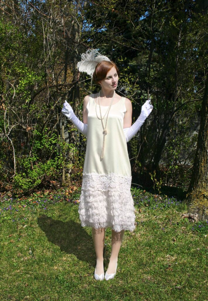 Woman wearing white flapper dress standing in a field. 