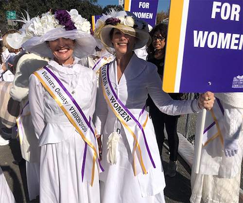 Two participants dressed up for the parade in Edwardian suits and hats with suffrage sashes and signs