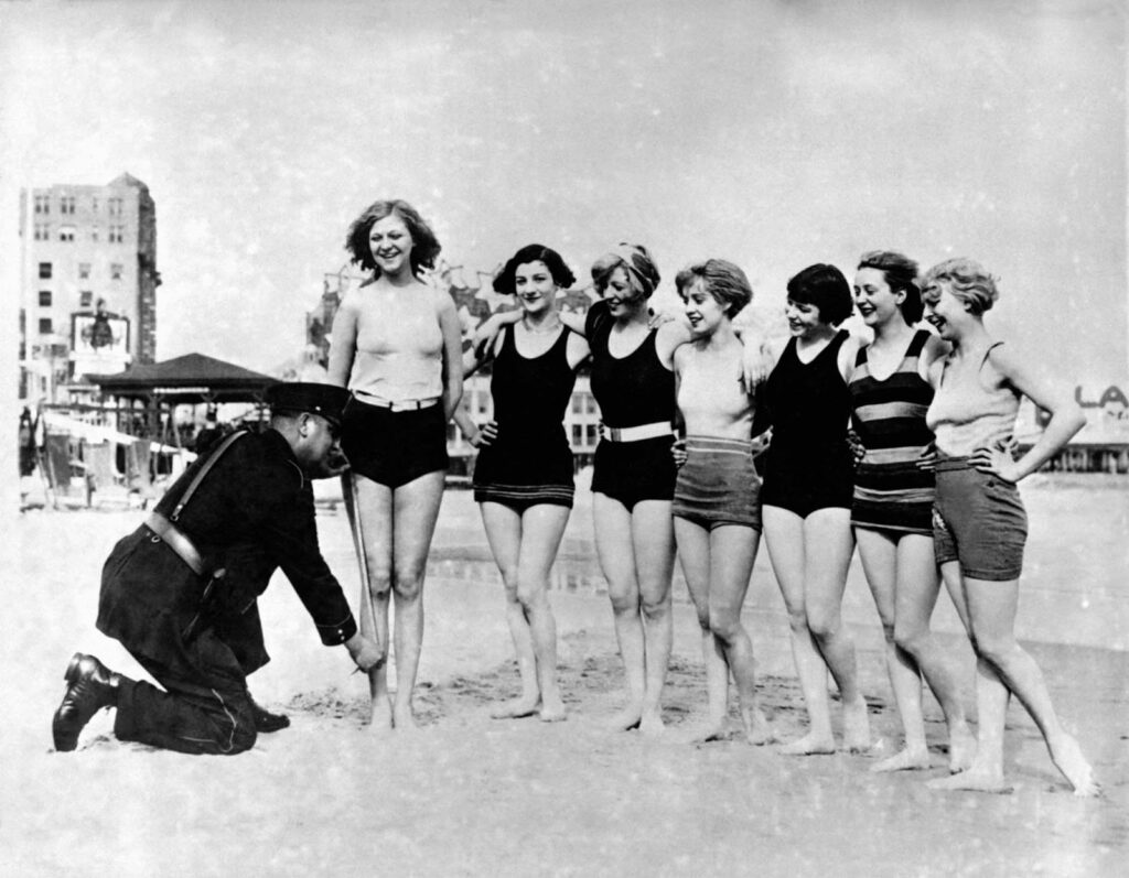 1920s WOMAN IN BATHING SUIT COSTUME STANDING ON BEACH PUTTING BAIT